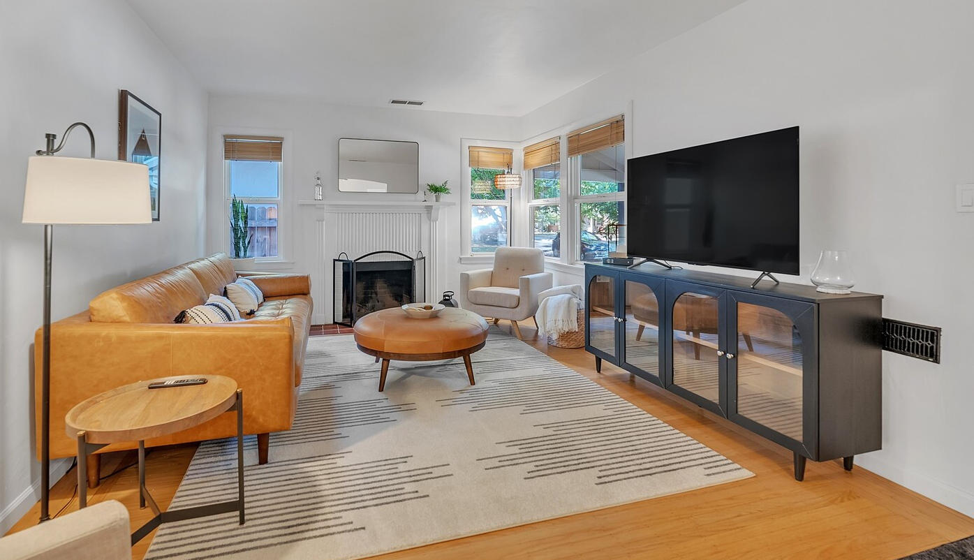 This mid-century modern family room exudes timeless elegance with its open layout, featuring a sleek black media console housing with SmartTV. The low-profile genuine leather sofa, paired with classic accent chairs, offers comfortable seating. A stylish ge